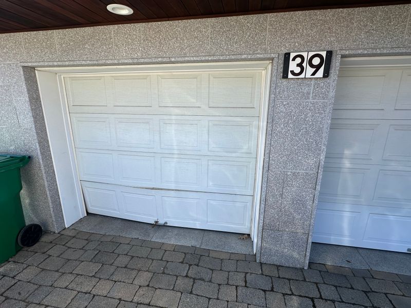 Damaged white raised-panel garage door misaligned in frame before repair